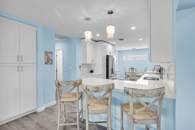 kitchen with sink, white cabinets, stainless steel fridge, a kitchen bar, and hanging light fixtures