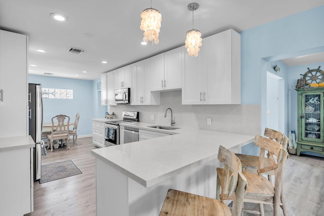 kitchen featuring sink, white cabinets, hanging light fixtures, kitchen peninsula, and stainless steel appliances