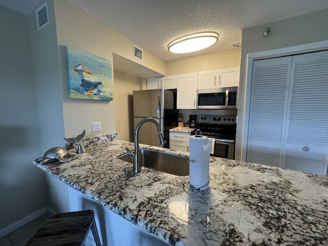 kitchen with white cabinetry, a sink, visible vents, stainless steel appliances, and stone counters