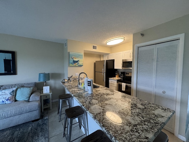 kitchen with a sink, a breakfast bar area, stone counters, a peninsula, and appliances with stainless steel finishes