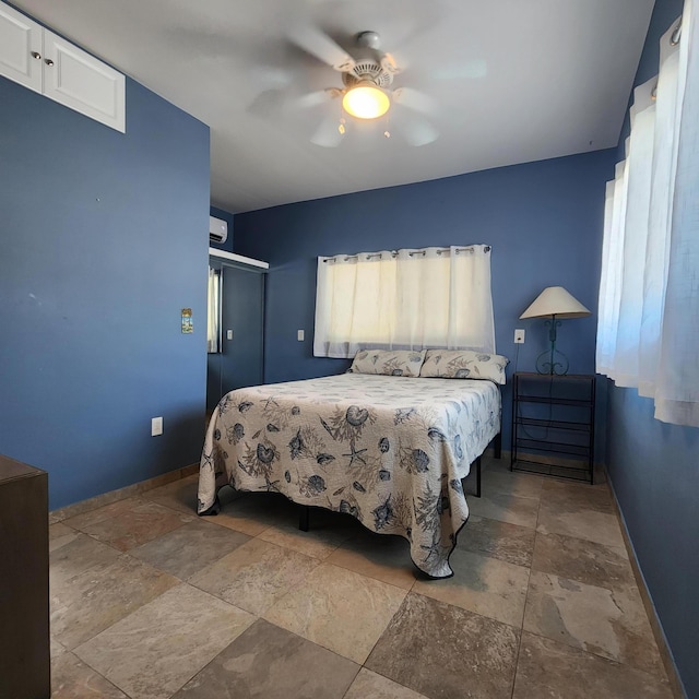 bedroom featuring stone tile floors, a ceiling fan, baseboards, and a closet