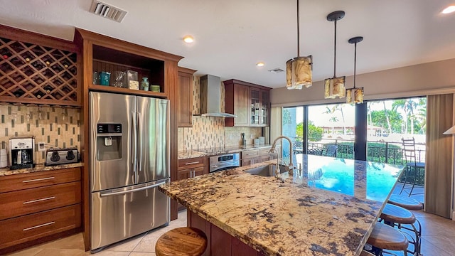 kitchen with sink, wall chimney range hood, a breakfast bar, appliances with stainless steel finishes, and light stone counters