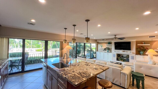 kitchen with sink, dishwasher, a kitchen island with sink, light stone counters, and decorative light fixtures