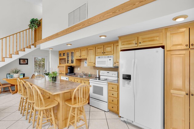 kitchen featuring a breakfast bar, a high ceiling, a center island, light tile patterned floors, and white appliances