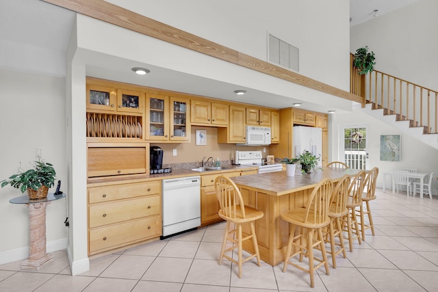 kitchen featuring sink, a kitchen breakfast bar, a center island, light tile patterned floors, and white appliances