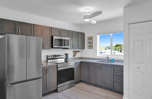 kitchen with light stone counters, light wood-style flooring, a sink, ceiling fan, and stainless steel appliances