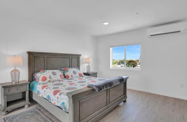 bedroom featuring light wood-style floors, baseboards, and a wall mounted AC