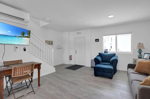 living area featuring stairway, light wood finished floors, and a wall mounted air conditioner