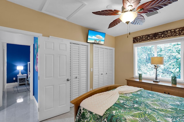 bedroom with light tile patterned flooring, two closets, and ceiling fan