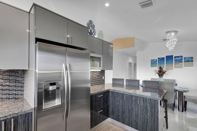 kitchen with kitchen peninsula, stainless steel fridge with ice dispenser, a breakfast bar area, and dark stone countertops