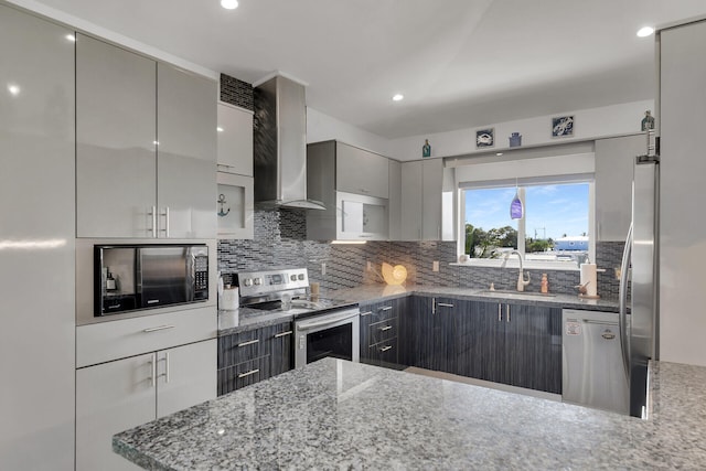 kitchen featuring wall chimney exhaust hood, sink, dark stone countertops, stainless steel appliances, and decorative backsplash