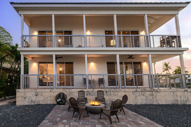 back house at dusk featuring ceiling fan, a balcony, an outdoor fire pit, and a patio area