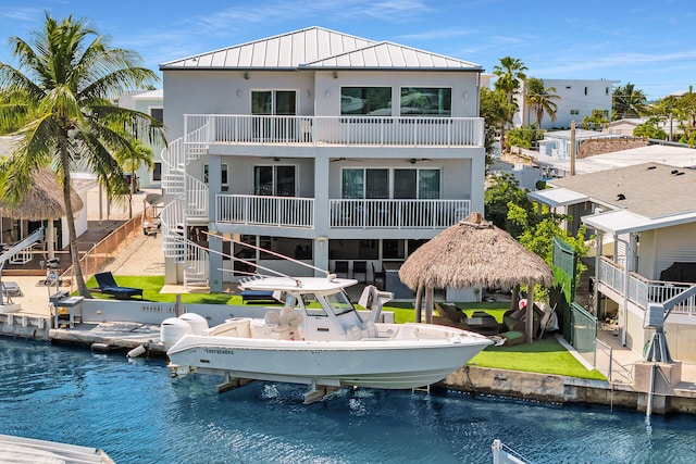 rear view of property featuring boat lift, a water view, stairs, stucco siding, and a standing seam roof