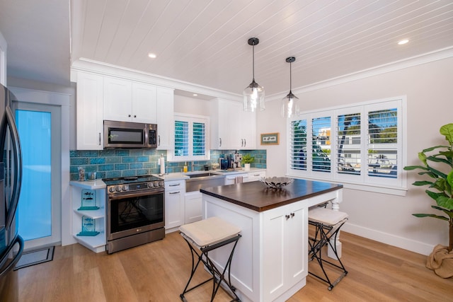 kitchen with a breakfast bar, appliances with stainless steel finishes, hanging light fixtures, white cabinets, and a kitchen island