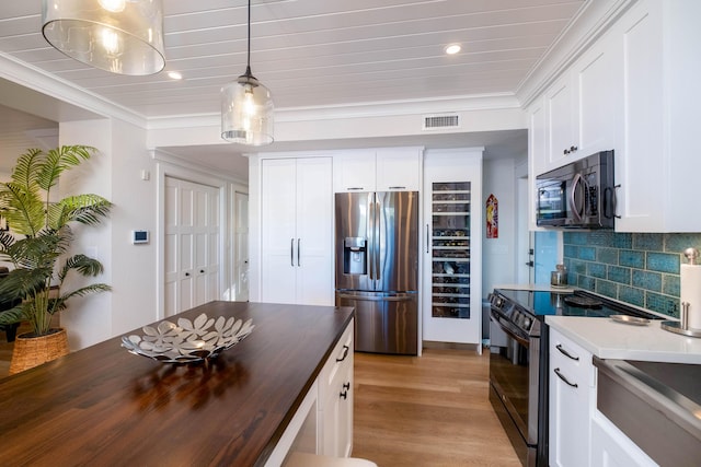 kitchen featuring white cabinetry, appliances with stainless steel finishes, decorative light fixtures, and butcher block countertops