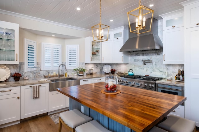 kitchen featuring white cabinets, dark stone counters, hanging light fixtures, stove, and wall chimney range hood