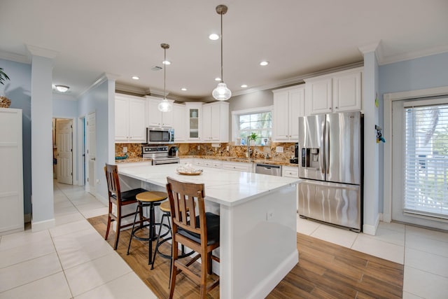 kitchen with hanging light fixtures, white cabinetry, appliances with stainless steel finishes, and crown molding