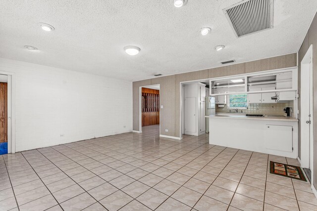 unfurnished living room with brick wall and a textured ceiling