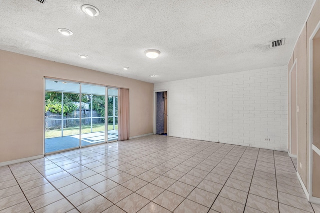 tiled empty room with a textured ceiling and brick wall