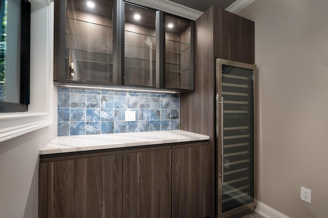 bar with dark brown cabinets, light stone counters, wine cooler, and backsplash