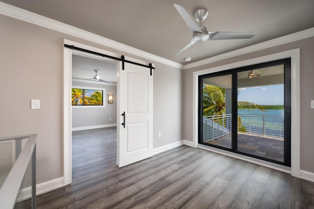 empty room featuring ceiling fan, ornamental molding, a barn door, and hardwood / wood-style floors