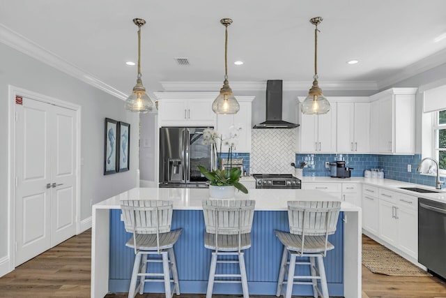 kitchen with a kitchen island, appliances with stainless steel finishes, light countertops, wall chimney range hood, and a sink
