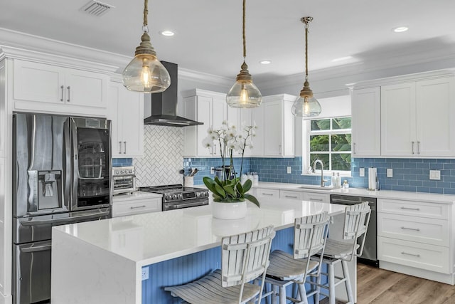 kitchen featuring stainless steel appliances, decorative light fixtures, a kitchen island, and wall chimney exhaust hood