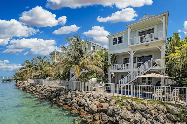 rear view of property featuring a water view, a balcony, fence, and a pool