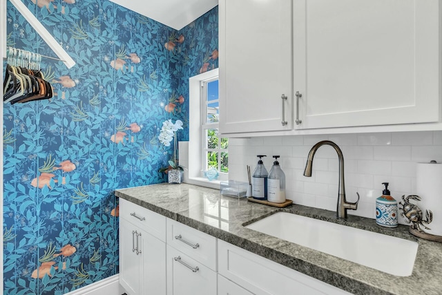 kitchen featuring wallpapered walls, dark stone counters, white cabinets, and a sink