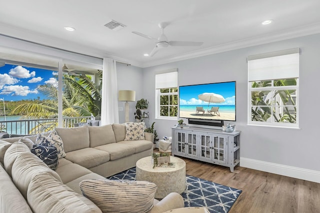 living room with ornamental molding, wood finished floors, visible vents, and a ceiling fan