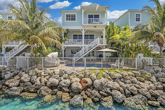 back of property with stairway, a swimming pool, fence, and a balcony