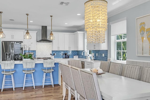 kitchen with hanging light fixtures, wall chimney range hood, light countertops, and a center island