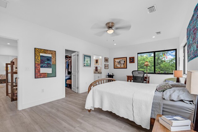 bedroom featuring light hardwood / wood-style flooring, ceiling fan, ensuite bathroom, a walk in closet, and a closet