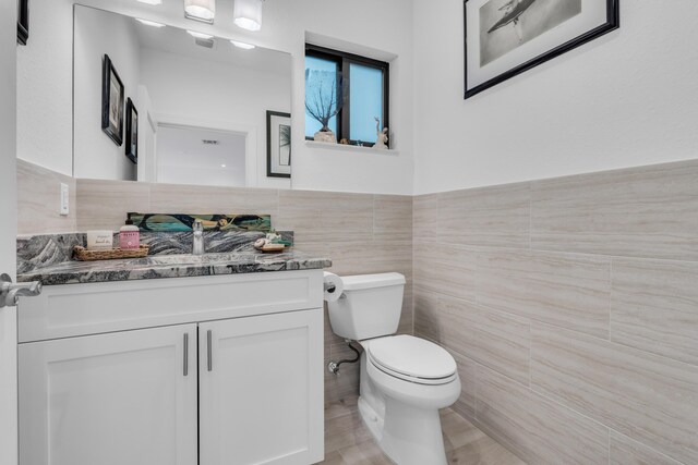 bathroom featuring vanity, tile walls, and toilet