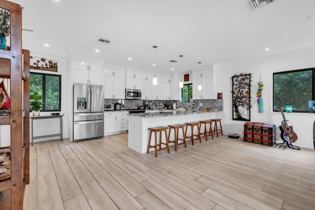 kitchen featuring appliances with stainless steel finishes, tasteful backsplash, white cabinetry, light stone counters, and kitchen peninsula