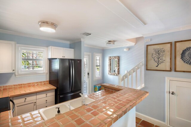 kitchen featuring white cabinetry, black fridge, ornamental molding, and tile counters