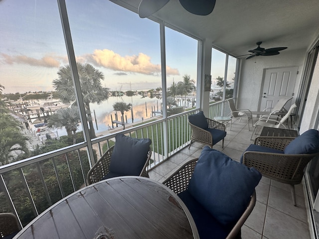 balcony at dusk featuring a water view and ceiling fan