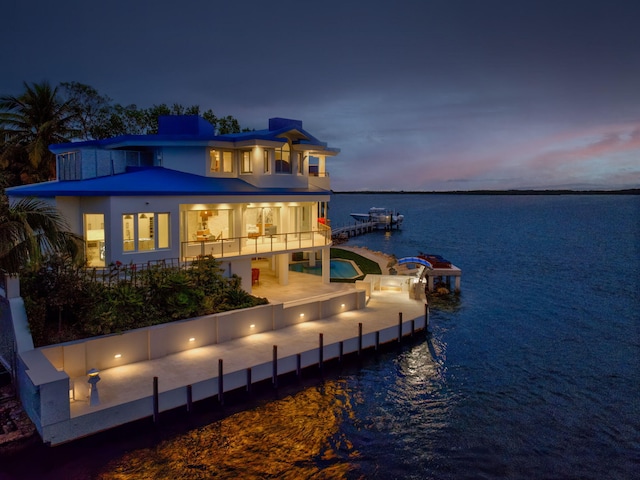 back house at dusk featuring a patio, a balcony, and a water view