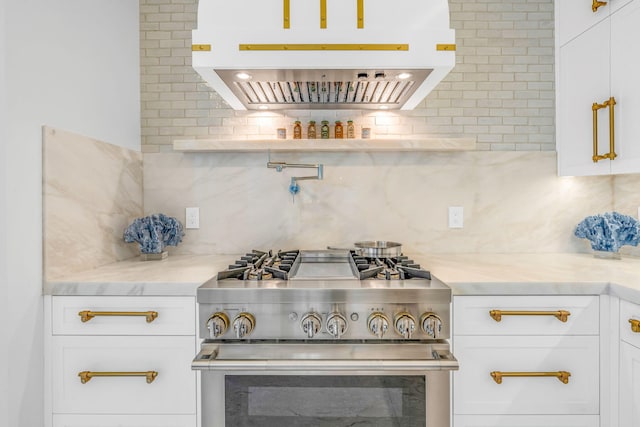 kitchen with extractor fan, high end stove, light stone countertops, white cabinets, and decorative backsplash