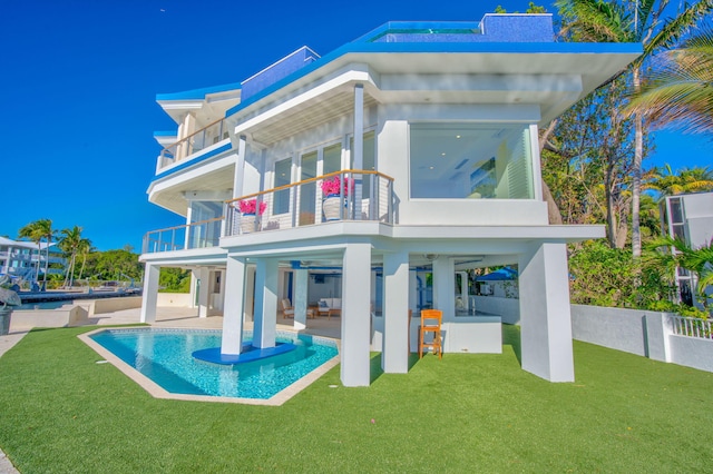 rear view of house with ceiling fan, a balcony, a yard, and a patio