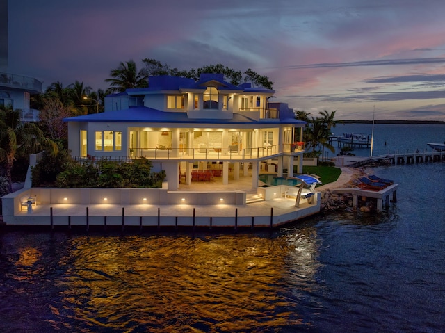 back house at dusk featuring a pool, a patio area, a balcony, and a water view