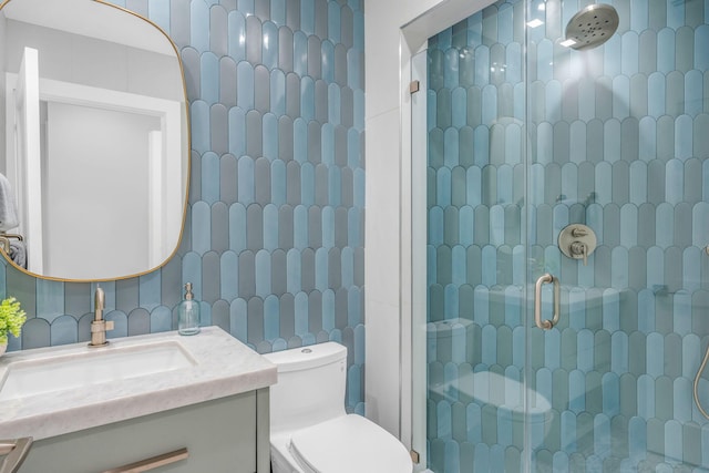 bathroom featuring toilet, tile walls, vanity, a shower with door, and decorative backsplash