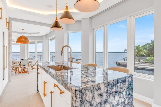 kitchen with pendant lighting, white cabinetry, sink, dark stone counters, and a water view