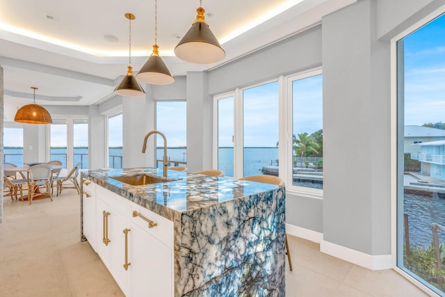 kitchen with pendant lighting, dark stone counters, white cabinets, and a water view