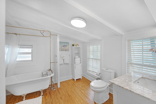 bathroom featuring vaulted ceiling with beams, a freestanding tub, toilet, wood finished floors, and plenty of natural light