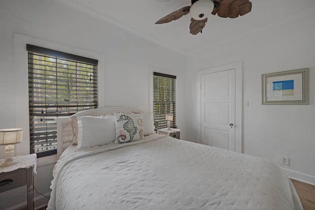 bedroom with ornamental molding, multiple windows, baseboards, and wood finished floors