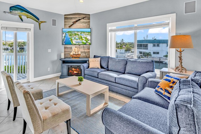living area featuring a warm lit fireplace, a water view, marble finish floor, visible vents, and baseboards