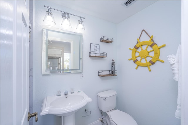 half bath with visible vents, toilet, baseboards, and a sink