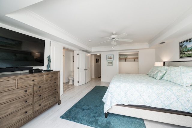 bedroom with ornamental molding, ceiling fan, light wood-type flooring, and a tray ceiling