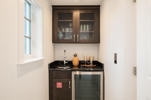 bar with wine cooler, sink, dark brown cabinets, and dark stone countertops